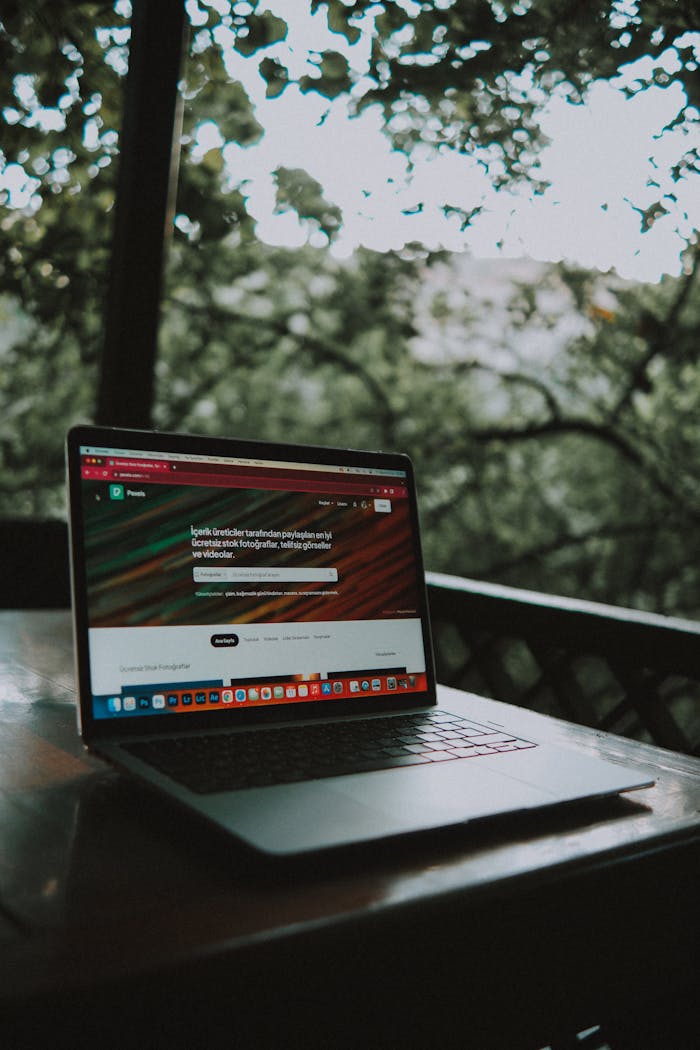 brand-03 Open laptop showing a website screen on a wooden table in an outdoor terrace setting.