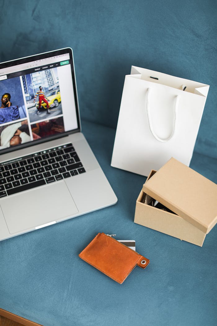 creative-01 A high-angle view of online shopping items including a laptop, gift bags, and wallet on a blue surface.